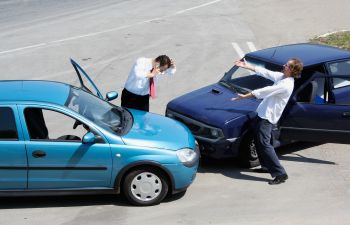 Two stressed businessmen arguing after traffic collision by their damaged cars damaged.