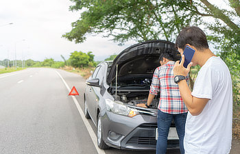 friends fixing car broken down on highway calling for help on mobile phone