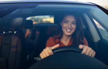 Happy woman driving a car and smiling. Cute young success happy brunette woman is driving a car. Portrait of happy female driver steering car with safety belt
