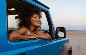 Image of cheerful african american woman smiling while travelling in car on desert